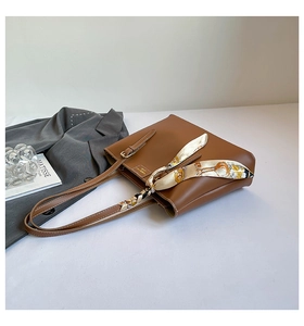 Detail of a brown leather tote bag with decorative silk scarf and long shoulder strap