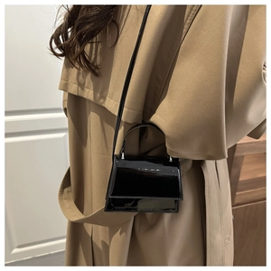 Close-up of a glossy black patent leather mini crossbody bag styled with a khaki trench coat
