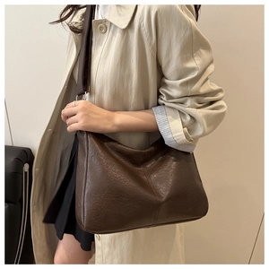 Détail d'un grand sac cabas en cuir grainé marron foncé avec large bandoulière porté