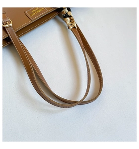 Detailed macro view of brown leather bag with white stitching and silk scarf wrap