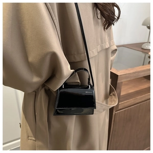 Side view of a black patent leather mini crossbody bag styled with a tan trench coat