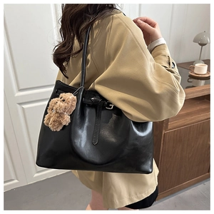Close-up of black matte leather tote bag with a cute brown plush bear charm and buckle