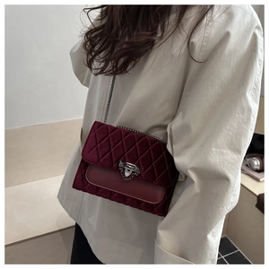 Close-up of wine red velvet crossbody bag with quilted pattern and metal chain strap