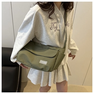 Green canvas crossbody bag with flap and fashion label worn by model in casual outfit