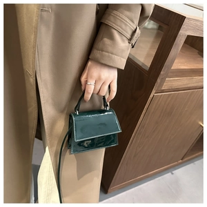 Detail of dark green patent leather mini handbag with glossy finish and top handle