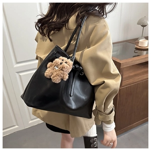 Detail of minimalist black faux leather tote bag featuring a brown teddy bear pendant