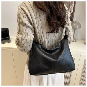 Détail du sac cabas croissant en cuir noir mat porté à l'épaule dans un décor de bureau