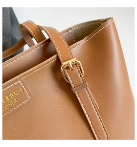 Detail of brown leather tote bag with gold buckle fastener and white contrast stitching