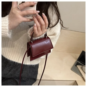 Detail of burgundy patent leather mini bag held by hand, showing shiny finish and metal clips