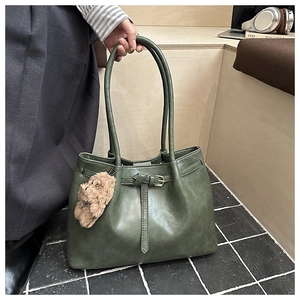 Detail of dark green leather tote bag with gold buckle and cute plush bear charm