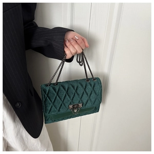 Detail of dark green velvet crossbody bag showing quilted texture and metal chain