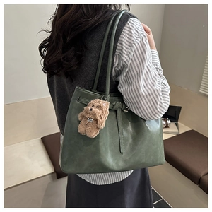 Detail of dark green matte tote bag with thin shoulder straps and a plush bear pendant