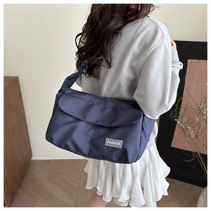 Detail view of the navy blue messenger bag worn by a model in a casual indoor setting
