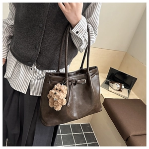 Detail of a large brown tote bag featuring matte leather and a cute plush dog pendant