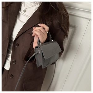 Close-up of a mini grey patent leather crossbody bag with metallic silver hardware details