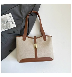 Detail of beige canvas tote bag with brown leather trim and golden twist lock closure