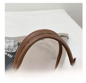 Detailed close-up of brown leather tote bag with thick rounded handles and fine stitching