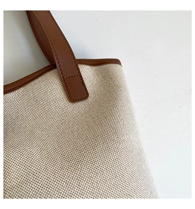 Detail of off-white woven canvas texture and brown leather stitching on tote bag