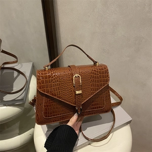 Brown crocodile embossed leather handbag with gold metal clasp on a reflective pedestal