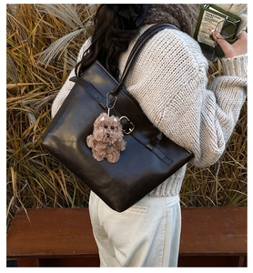 Deep brown leather tote bag with plush charm shown in a warm autumn outdoor setting