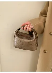 Borsa a mano marrone lucida a rilievo con dettagli dorati abbinata a cappotto beige