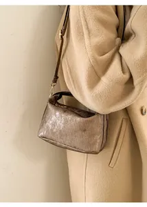 Close-up of metallic bronze pleated crossbody bag with gold hardware and beige coat