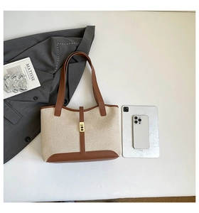 Detail of canvas tote bag with brown leather trim, metal buckle and tablet for size scale