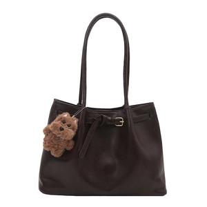 Deep brown leather tote bag with gold buckles and a cute plush dog charm on white background