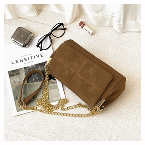 Detail of brown suede crossbody bag with decorative cross-stitching and gold chain strap