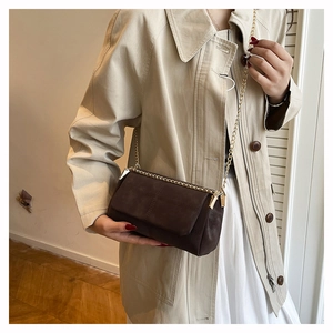 Detail of a brown suede messenger bag with gold chain strap on a model in trench coat