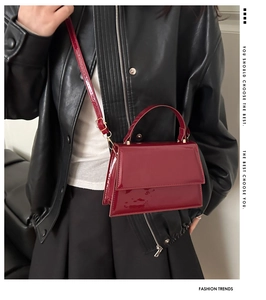 Détail d'un sac à bandoulière en cuir verni bordeaux brillant avec boucles dorées