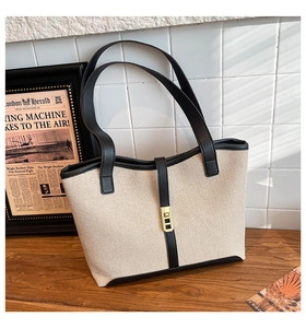 Detail shot of canvas tote bag with black leather trim and gold magnetic closure on desk