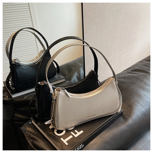 Detail view of crescent underarm bags in black and silver leather on a leather sofa