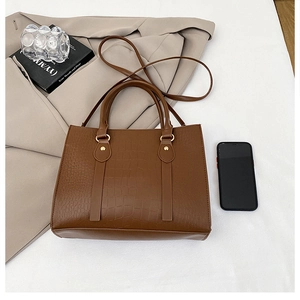 Detail of brown crocodile pattern tote bag with dual handles and detachable shoulder strap