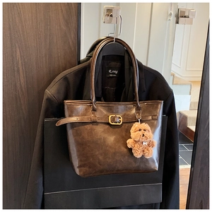 Detail of dark brown glossy tote bag featuring a gold buckle and plush puppy charm