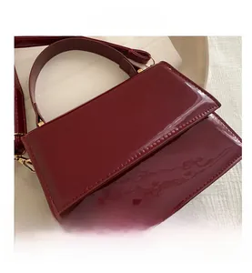 Gros plan d'un sac en cuir verni bordeaux avec poignée polie et boucle métallique chic
