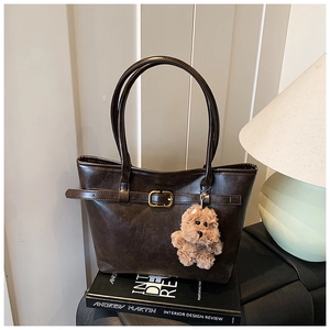 Detail of dark brown tote bag with retro leather texture, gold buckles and teddy bear charm