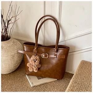 Detail of a brown faux leather tote bag with vintage metal buckles and a plush dog charm