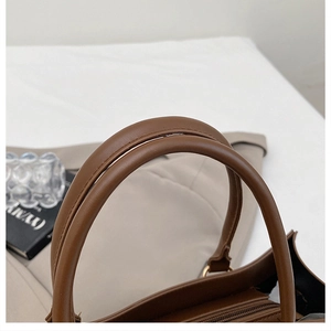 Detailed macro view of dark brown leather handbag handles and golden metal zipper hardware
