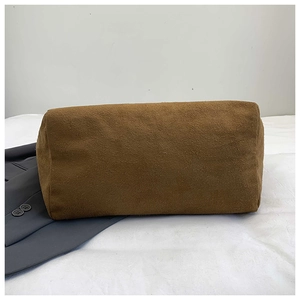 Detail shot of a brown suede cylindrical cosmetic bag on a textured white fabric surface