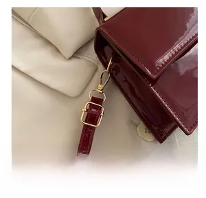 Détail rapproché des crochets dorés et de la bandoulière en cuir verni rouge du sac