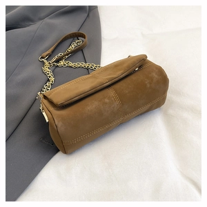 Detailed close-up of brown suede cylinder bag with double stitching and gold chain strap