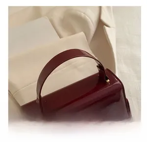 Détails du sac à main en cuir verni bordeaux avec poignée incurvée et bandoulière fine