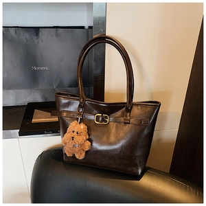 Detailed view of brown leather tote bag featuring golden metal buckle and cute bear charm