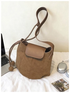 Détail d'un sac seau en daim marron avec rabat en cuir et cordon près d'un ordinateur