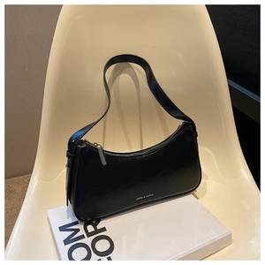 Close-up of black leather half-moon underarm bag with zipper detail on a book