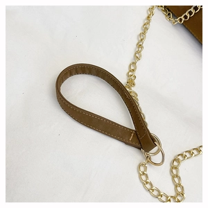 Close-up of brown leather handle with fine stitching and golden chain on shoulder bag