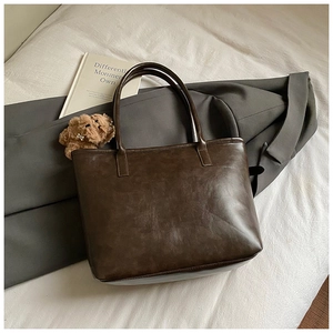 Close-up of a dark coffee leather tote bag with a cute brown plush bear charm detail