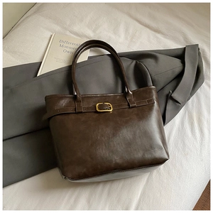 Close-up of deep coffee tote bag featuring matte leather texture and gold buckle detail