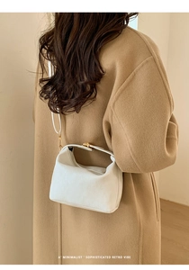 Detailed view of white ribbed texture handbag with elegant gold metal lock on camel coat